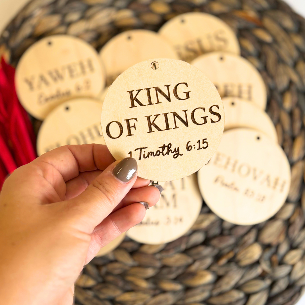 Hand holding a wooden round ornament with 'King of Kings' text, surrounded by similar ornaments.