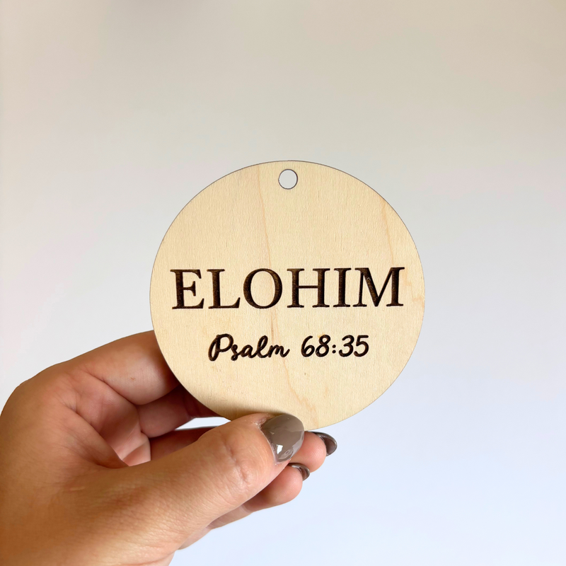 Round wooden sign with 'ELOHIM Psalm 68:35' text held by a hand against a light background