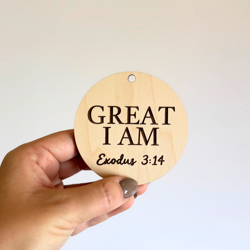 Round wooden ornament with 'GREAT I AM Exodus 3:14' text held by a hand against a light background