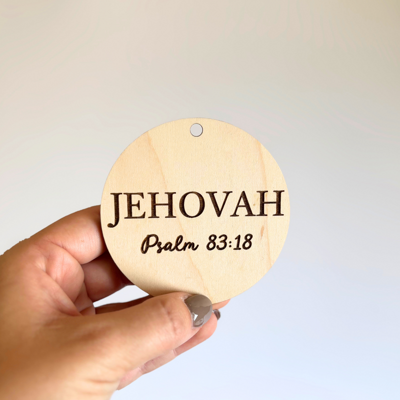 Hand holding a round wooden sign with 'Jehovah Psalm 83:18' text against a light background
