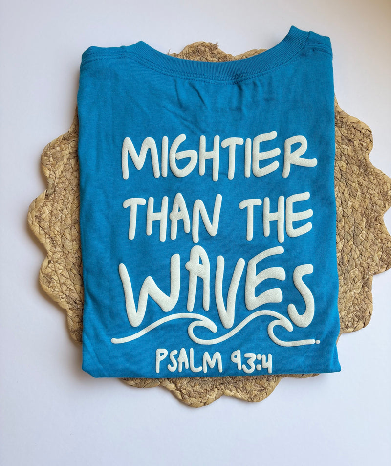 Blue kids t-shirt with 'Mightier Than The Waves' text on a textured surface