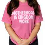 Person wearing a pink t-shirt with 'MOTHERHOOD IS KINGDOM WORK' text.