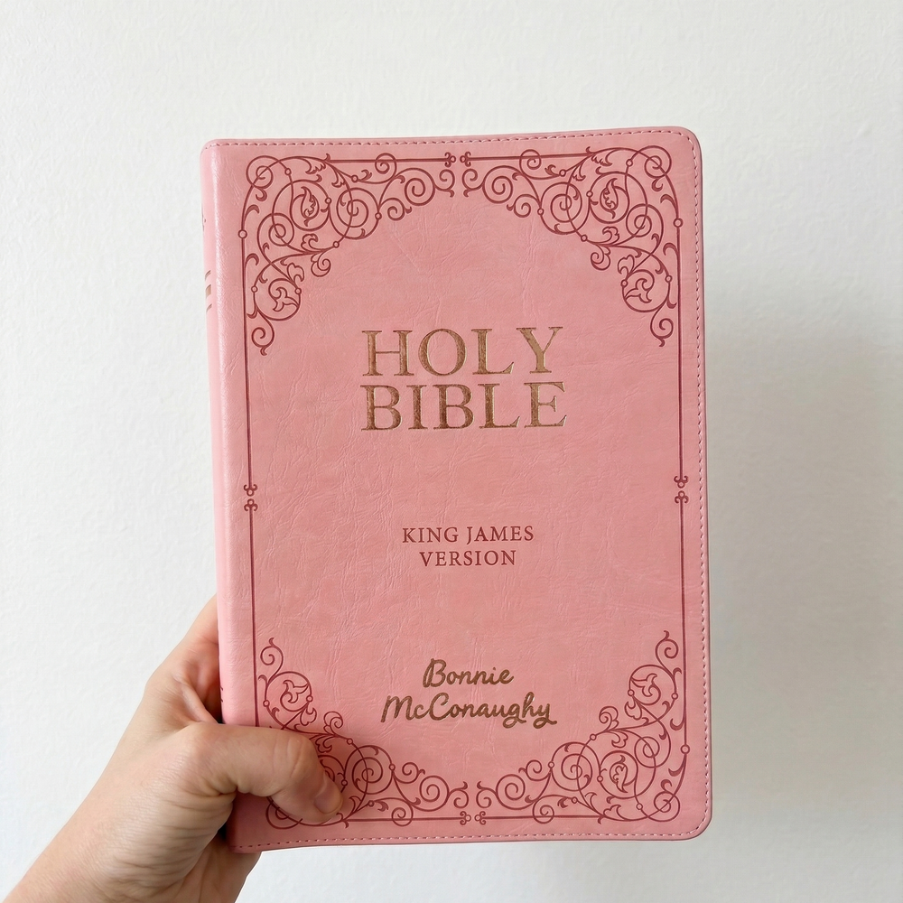Pink Bible with decorative cover held by a hand on a light background